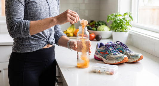 Person mixing electrolyte powder into a water bottle beside running shoes and a supplement case