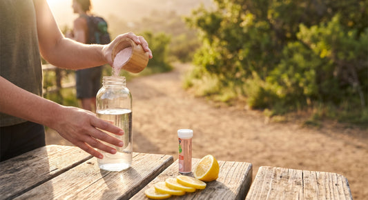 Person mixing an electrolyte drink outdoors beside electrolyte tablets and pink salt powder